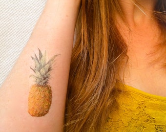 May include: A temporary tattoo of a yellow pineapple with green leaves on a person's arm.