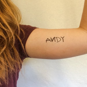 May include: A close-up of a person's arm with a temporary tattoo that says "ANDY" in black ink.