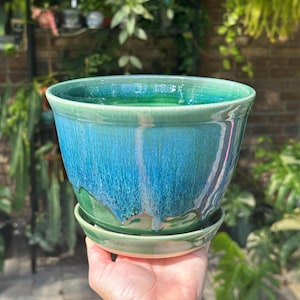 May include: A ceramic plant pot with a glossy finish featuring a vibrant gradient of deep ocean blue and forest green. The pot has a wide, flared rim and sits securely on a matching circular saucer, showcasing a smooth, glazed texture throughout.