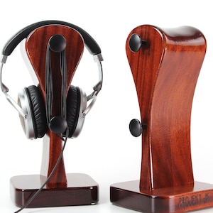 May include: Two wooden headphone stands with a rich, dark finish. One stand holds silver and black headphones. The stands have a curved design with black knobs for cable management. The base of one stand has the text "PROJECT JK".