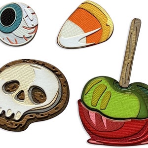 Puede incluir: Cuatro decoraciones de Halloween: un caramelo de maíz, una manzana verde con un recubrimiento de caramelo rojo, una calavera con detalles marrones y blancos y un ojo azul con un iris blanco.