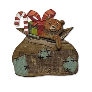 Puede incluir: Un saco de arpillera marrón con un osito de peluche, un bastón de caramelo y un regalo envuelto en su interior. El saco tiene parches azules con estrellas negras cosidas.