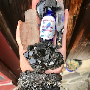May include: A small blue glass bottle with a dropper, labeled "Crystal Elixir Earth Star Activator". The bottle is surrounded by several black and clear crystals.