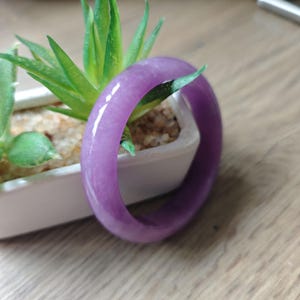 Op de afbeelding: Een gladde, gepolijste, doorschijnende paarse armband met een afgerond profiel. De armband heeft een consistente, levendige lavendeltint over de gehele massieve, cirkelvormige structuur en vertoont een glanzende, reflecterende oppervlakteafwerking.