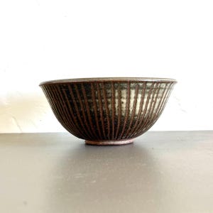 May include: A brown and white ceramic bowl with a ribbed design. The bowl is handmade and has a rustic look.