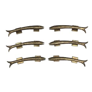 May include: Six gold-toned fish-shaped door handles with intricate details. The handles are mounted on a white background.
