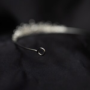 May include: A silver tiara with a delicate design of small, clear stones. The tiara has a simple, circular wire loop at the back for fastening.