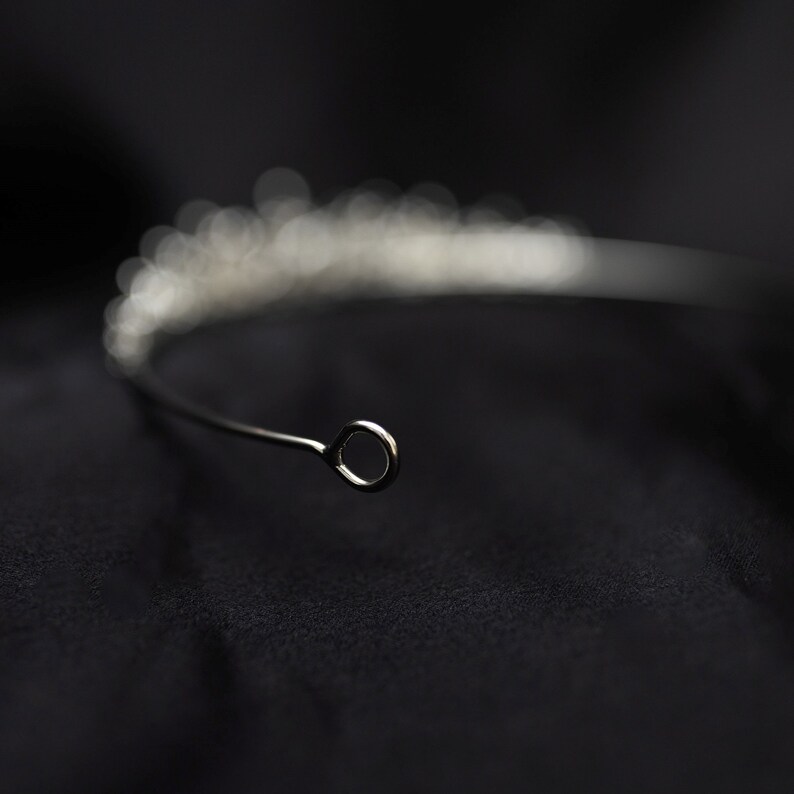 May include: A silver tiara with a delicate design of small, clear stones. The tiara has a simple, circular wire loop at the back for fastening.