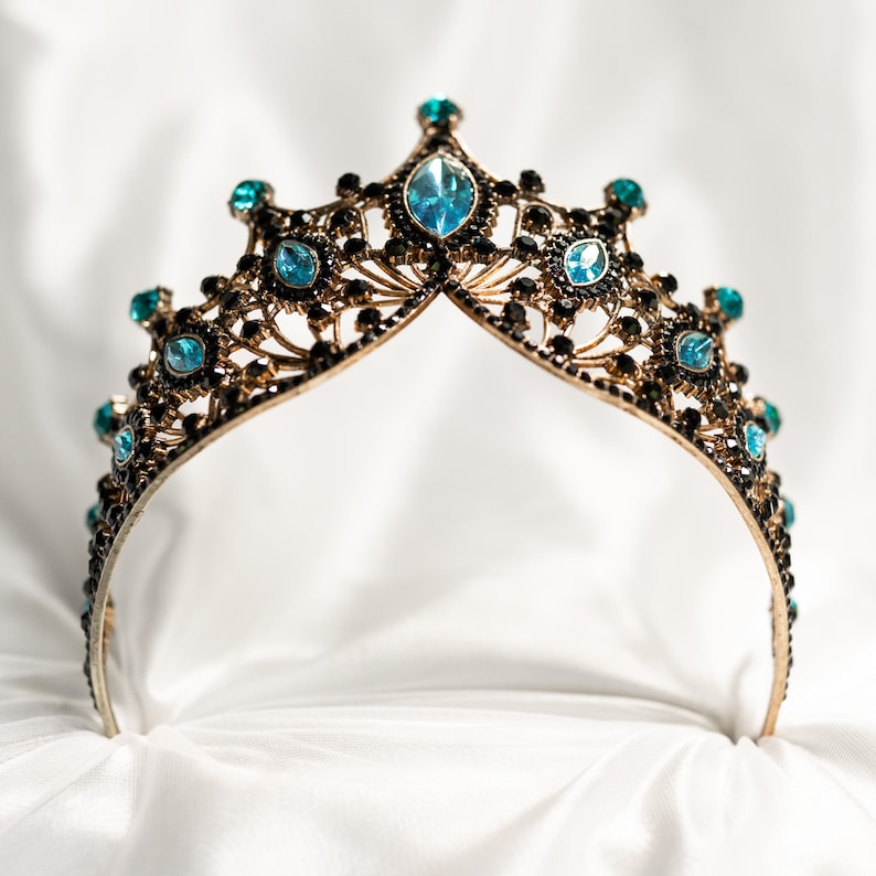 May include: A gold crown with blue gemstones and black accents. The crown is on a white background.