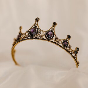 May include: A gold crown with purple gemstones and intricate detailing. The crown is on a white background.