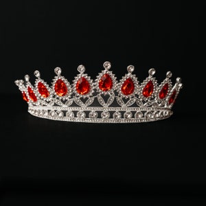 May include: A silver crown with red gemstones. The crown is decorated with smaller clear gemstones.