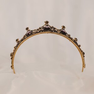 May include: A gold crown with purple gemstones and intricate details. The crown is on a white background.