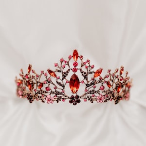 May include: A gold crown with a delicate floral design and red and pink gemstones.