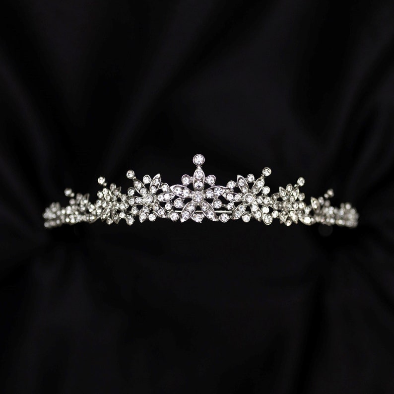 May include: A silver tiara with a row of clear rhinestones in a floral design.