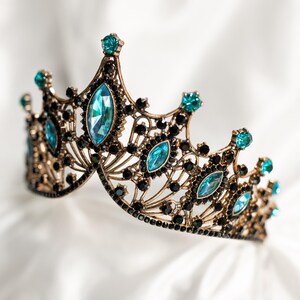 May include: A gold crown with black and blue gemstones. The crown is ornate and has a delicate design.