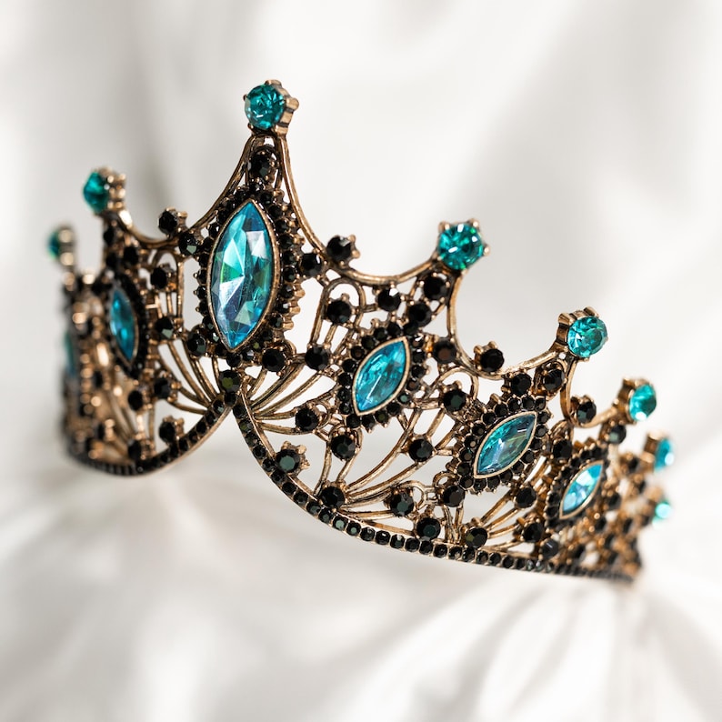 May include: A gold crown with black and blue gemstones. The crown is ornate and has a delicate design.