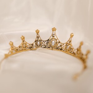May include: A gold crown with clear rhinestones, the crown is delicate and intricate with a filigree design.