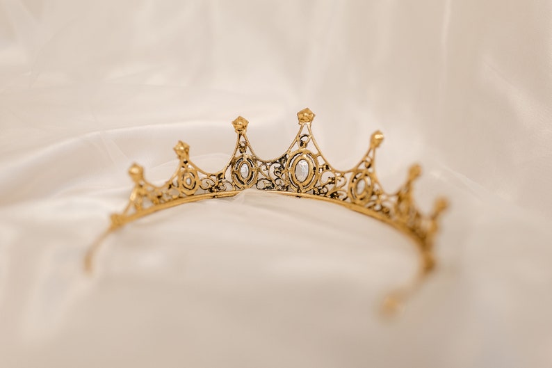 May include: A gold crown with clear rhinestones, the crown is delicate and intricate with a filigree design.