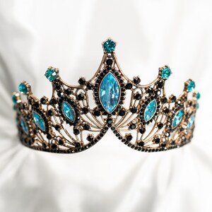 May include: A gold crown with a delicate design and blue gemstones. The crown is on a white background.