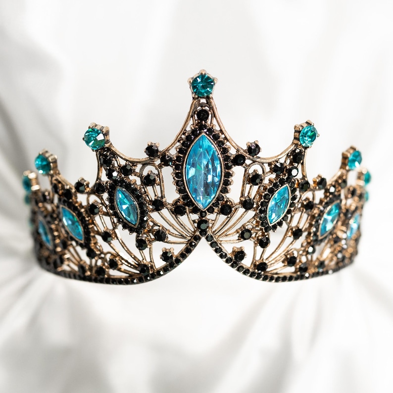 May include: A gold crown with a delicate design and blue gemstones. The crown is on a white background.