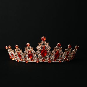 Peut inclure: Une couronne dorée avec des pierres précieuses rouges et claires. La couronne est sur un fond noir.