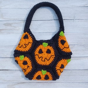 May include: A black and orange crocheted tote bag with a Halloween theme. The bag is decorated with pumpkin faces and green leaves.