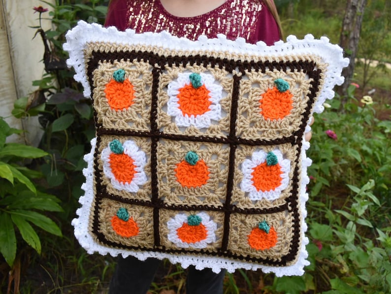 May include: A crocheted pillow with a brown, white, and orange pumpkin design. The pillow has a white crocheted border.