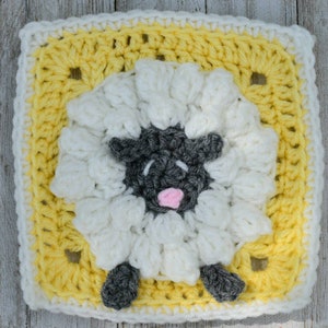 May include: A crocheted square featuring a white sheep with a black face and pink nose, surrounded by a yellow border.