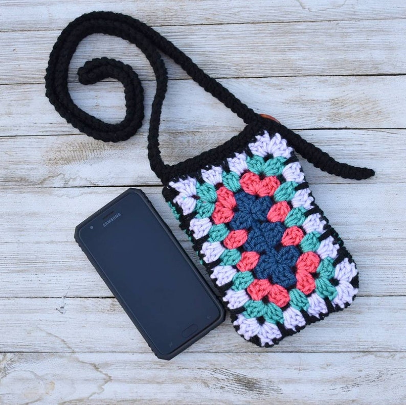 May include: A crocheted phone bag with a black strap and a colourful granny square design. The bag is made with pink, green, blue, and white yarn.