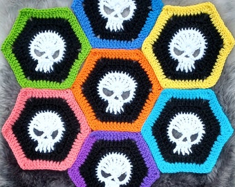 May include: A colorful crocheted hexagon wall hanging with a skull design in each section. The skulls are white with black eyes and are surrounded by a black outline. The hexagons are in shades of green, blue, yellow, orange, and purple.