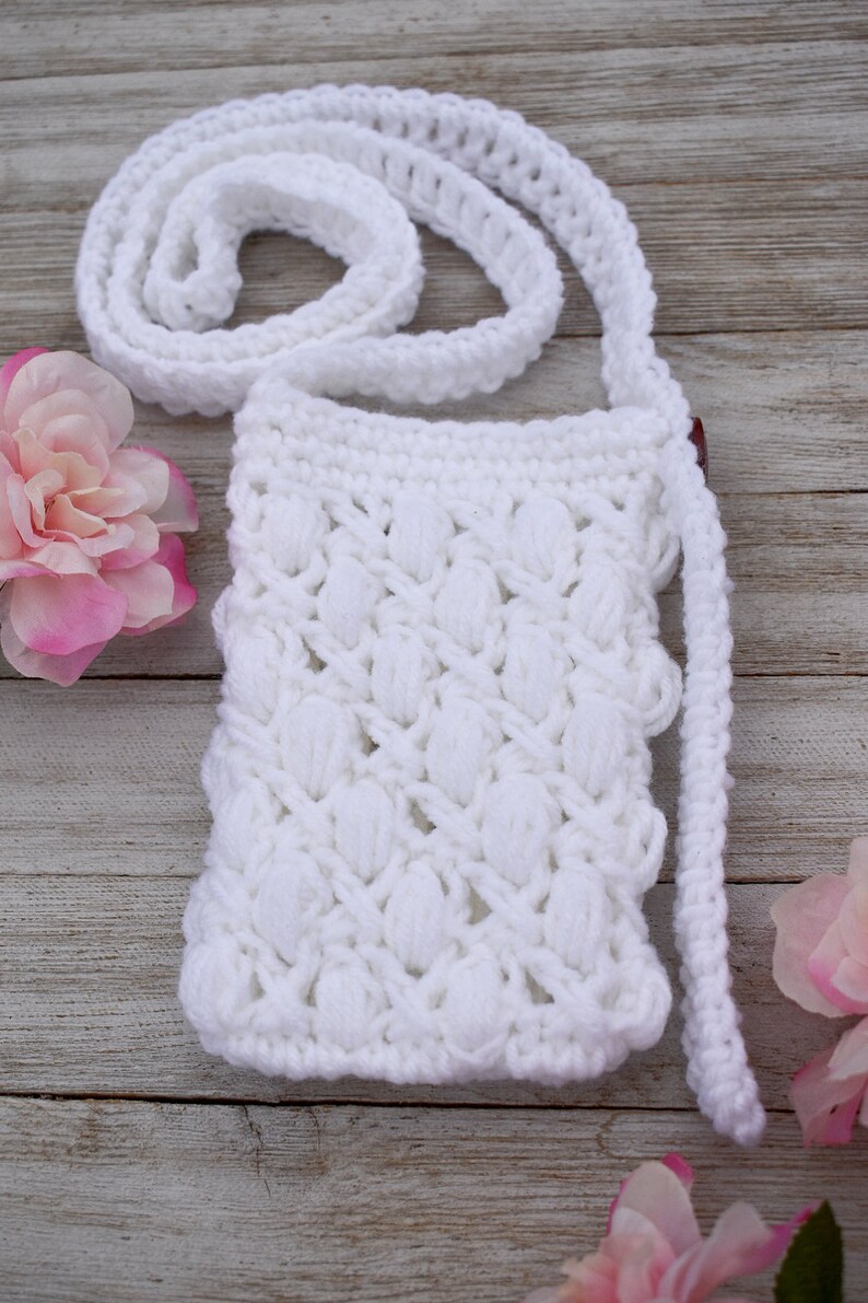 May include: White crocheted crossbody bag with a textured, puffy design. The bag has a long strap and is made with a white yarn.
