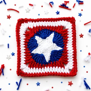 May include: A square crochet motif featuring a central white five-pointed star on a circular blue background, surrounded by concentric square layers of white and red yarn. The design uses a classic stitch pattern with a vibrant red, white, and blue color scheme.