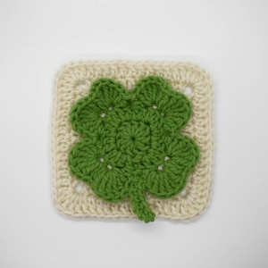 May include: A crocheted square with a green four-leaf clover design in the center.