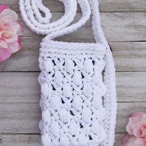 May include: White crocheted crossbody bag with a textured, puffy design. The bag has a long strap and is made with a white yarn.