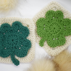 May include: Two crocheted four-leaf clover squares in green and white. The squares are made with a granny stitch pattern.