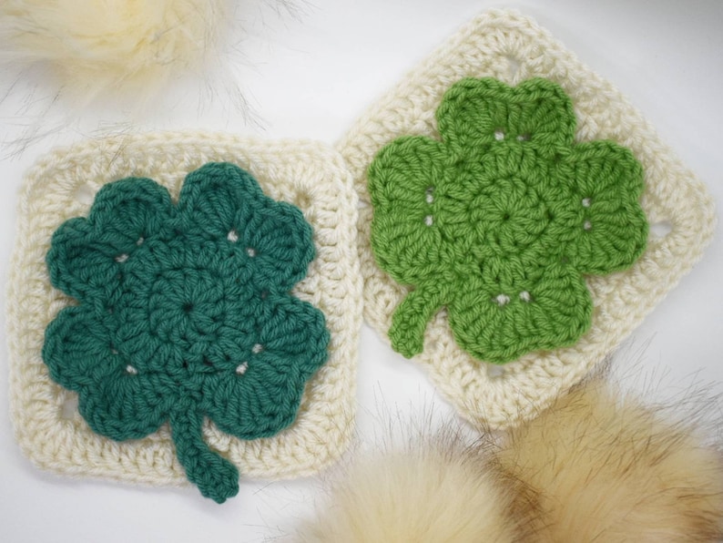 May include: Two crocheted four-leaf clover squares in green and white. The squares are made with a granny stitch pattern.
