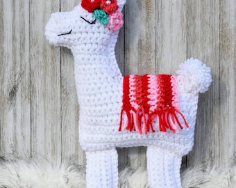 May include: White crocheted llama with a pink and red striped scarf and a flower crown with pink, red, and green flowers.