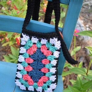 May include: A colourful crocheted granny square bag with a black strap. The bag is hanging on a blue wooden chair.