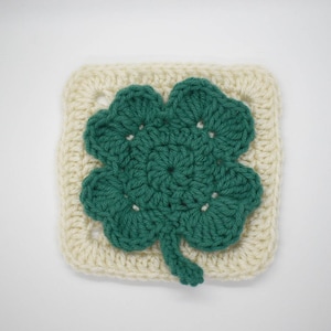 May include: A crocheted square with a green four-leaf clover design in the center.