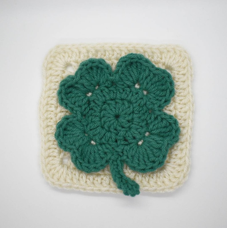 May include: A crocheted square with a green four-leaf clover design in the center.
