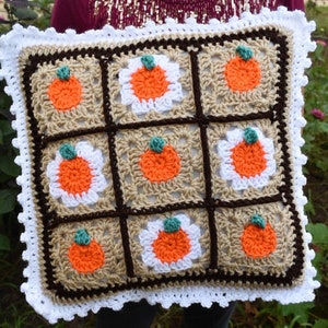 May include: A crocheted pillow with a brown and white checkered pattern and orange pumpkins. The pillow has a white crocheted border.