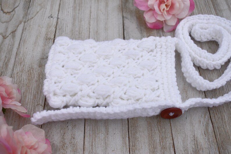 May include: White crocheted crossbody bag with a button closure and a long strap. The bag has a textured, puffy design.