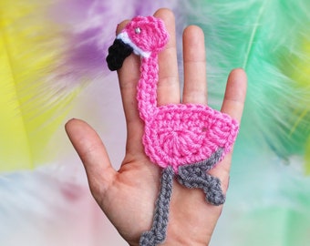 Puede incluir: Flamenco de crochet rosa con patas grises y pico negro. El flamenco está en una mano.