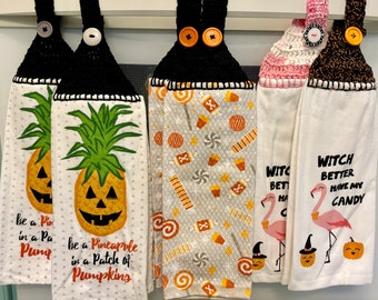 Puede incluir: Cinco paños de cocina decorativos con la parte superior de ganchillo y cierres de botón. Los paños presentan diseños temáticos de Halloween, incluyendo piñas jack-o'-lantern, patrones de caramelos y flamencos con sombreros de bruja. El texto en los paños dice "be a Pineapple in a Patch of Pumpkins" y "Witch Better Have My Candy."