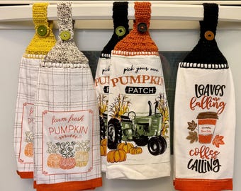 Puede incluir: Un conjunto de cinco paños de cocina colgantes con la parte superior de ganchillo en amarillo, gris, negro y naranja. Las toallas presentan diseños con temática otoñal, incluyendo calabazas, un tractor y las frases "farm fresh pumpkin" y "leaves are falling, coffee is calling."