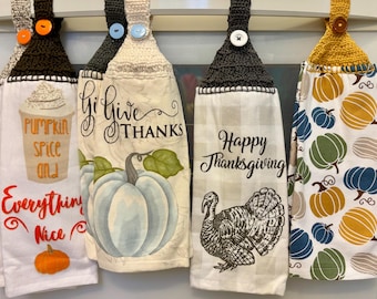 Puede incluir: Cuatro paños de cocina decorativos con la parte superior de ganchillo y cierres de botón. Los paños presentan diseños con temática otoñal, incluyendo calabazas, un pavo y las frases "Give Thanks" y "Happy Thanksgiving."