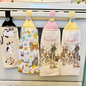 May include: Four kitchen towels with crocheted loops and buttons. Each towel features a different Easter-themed design with animals wearing bunny ears. The towels say "Happy Easter" on the bottom.