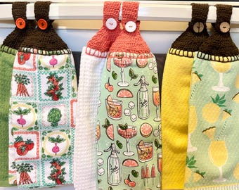 Puede incluir: Una colección de paños de cocina colgantes con la parte superior de ganchillo. Los paños presentan varios diseños, incluyendo verduras, cócteles y cítricos. Las partes superiores de ganchillo son marrones, coral y verdes, con cierres de botón.