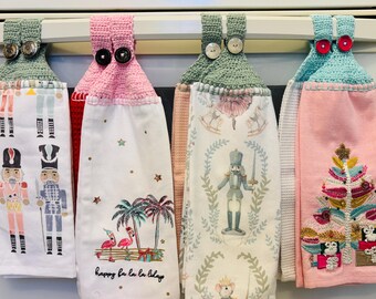 Puede incluir: Una colección de paños de cocina decorativos colgados de una estufa. Las toallas presentan varios diseños, incluyendo cascanueces, flamencos y un árbol de Navidad. Cada toalla tiene una parte superior de ganchillo con cierres de botón, en tonos verdes, rosas y azules.