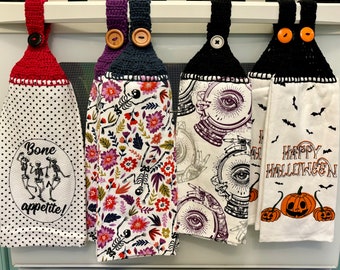 Puede incluir: Una colección de paños de cocina con temática de Halloween con la parte superior de ganchillo y cierres de botón. Los diseños incluyen esqueletos, estampados florales, bolas de cristal y calabazas. Un paño dice "Bone appetite!" y otro dice "Happy Halloween".